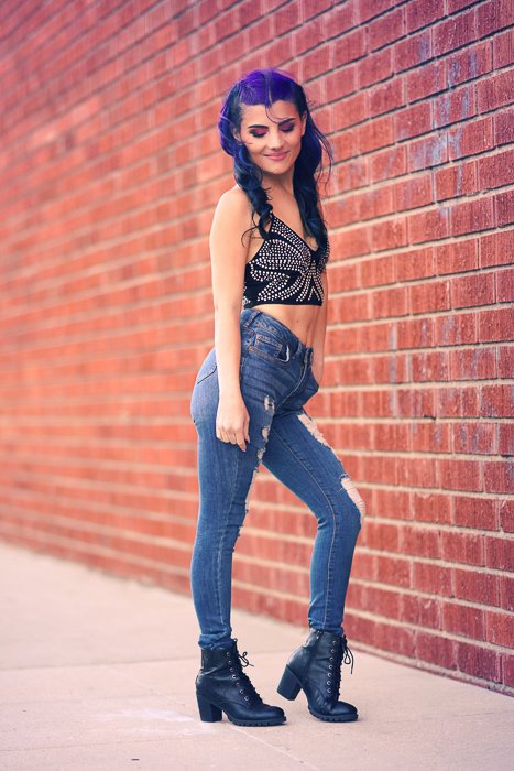 A portrait of a purple hair photography model posing by a brick wall