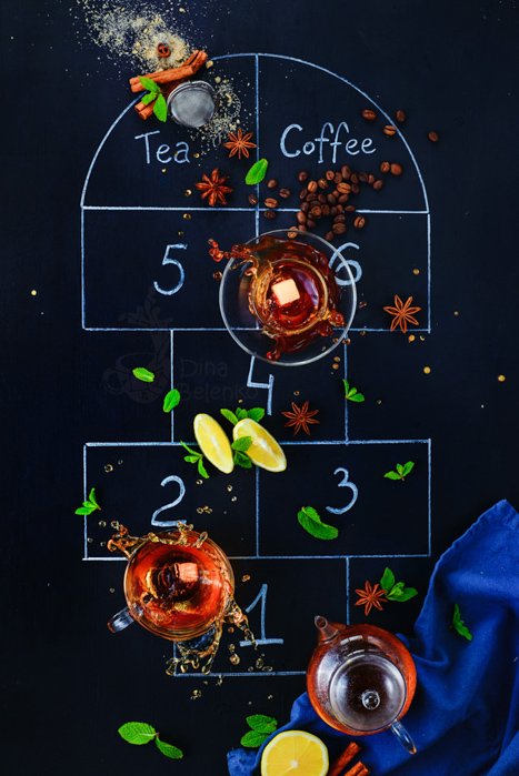A flat lay photo of tea cups and ingredients on a chalk hopscotch grid on a dark background - creative still life composition