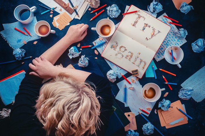 一个孩子靠在一张桌子上，桌子上放满了咖啡杯和文具，背景是黑色的，这是一幅创造性的静物构图