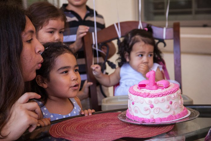 A little girl blowing out birthday candles on a cake at a family birthday party - birthday party photography