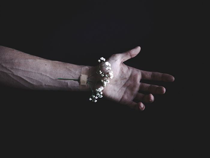 A dark and moody conceptual photo of a flower bandaged to a persons wrist 