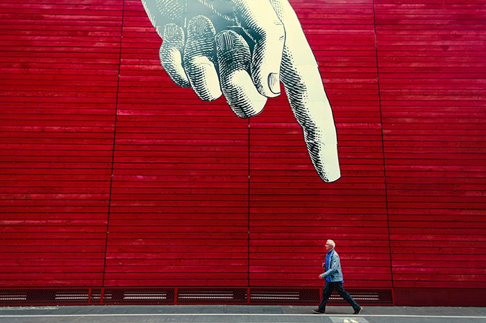 A conceptual photography shot of a man walking under a huge picture of a pointing finger