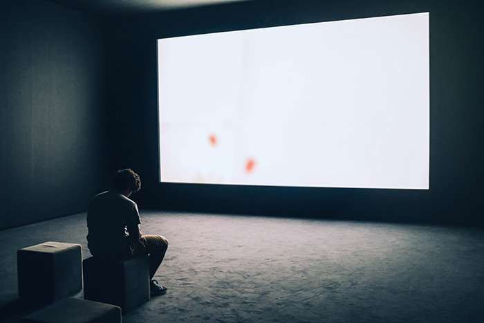 A conceptual self portrait of a man sitting in front of a large blank screen