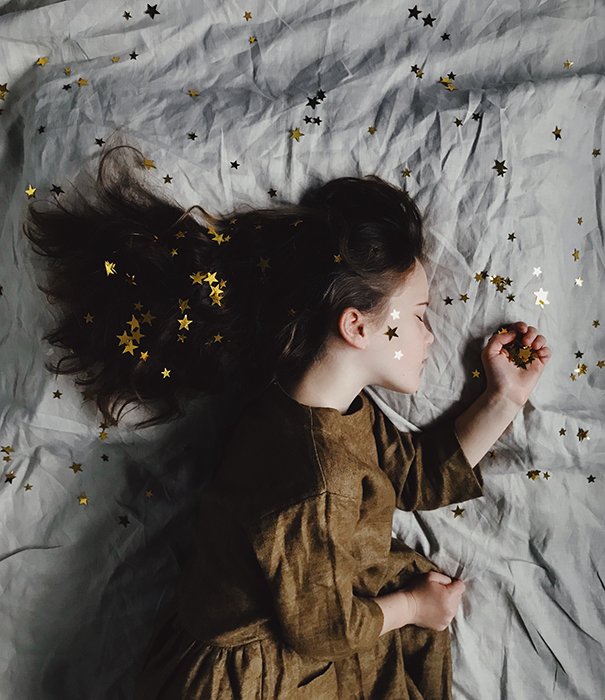 A dreamy conceptual portrait of a little girl sleeping, covered in golden stars