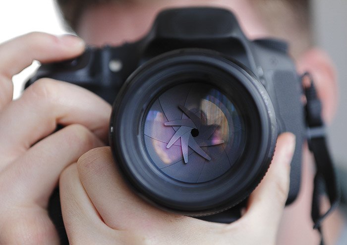 A close up of a photographer taking a shot with a DSLR to show the aperture - different camera parts