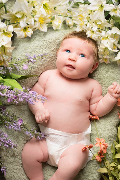 a Floral-Themed Easter photoshoot of a newborn surrounded by Easter-related objects like feathers, palms, and fake butterflies - easter photography ideas