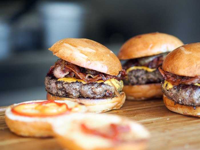 A close up shot of three hamburgers on a wooden board