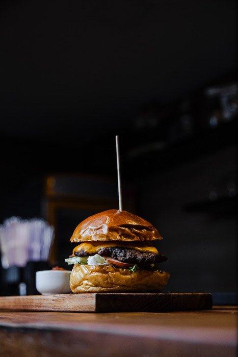A dark and moody shot of a hamburger on a wooden board - food photography examples
