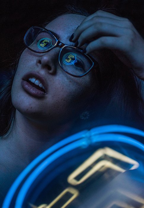 An atmospheric neon photography portrait of a female model with neon lights reflected in her glasses