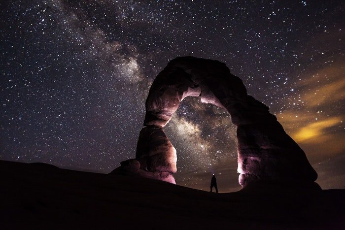 A stunning night photography image with a man under a stone arch and starry sky 