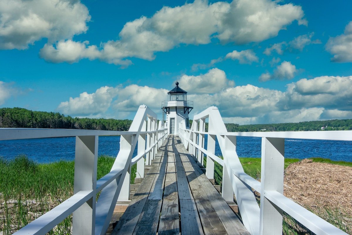 A white, wood walkway leading to a lighthouse and water