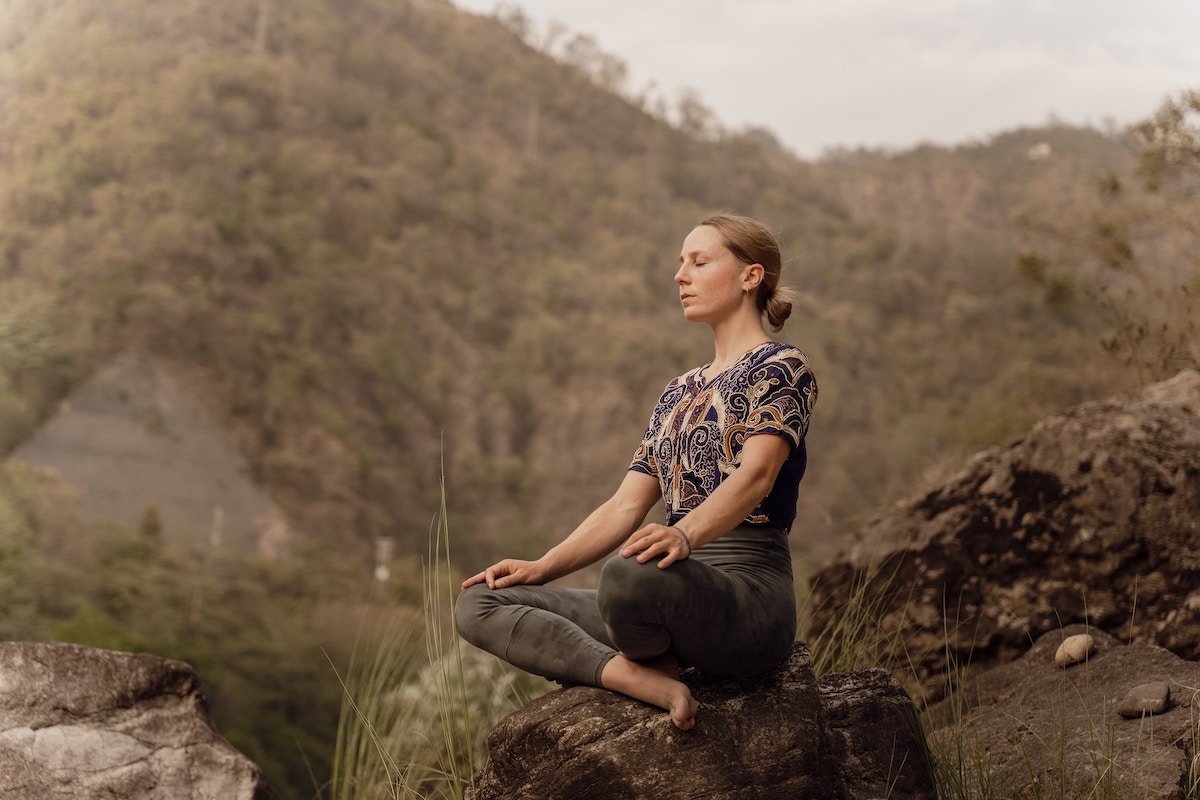 A woman sitting on a rock in nature meditating