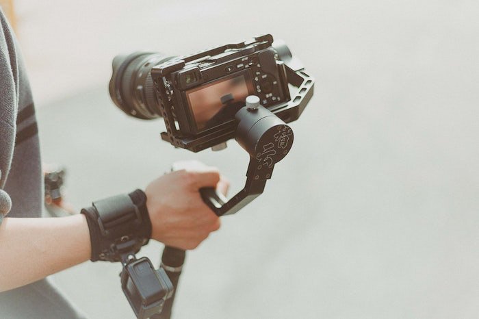 A bright and airy photo of a photographer holding a DSLR camera on a tripod