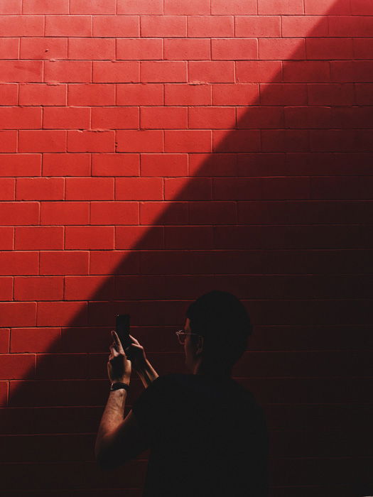 A man taking a smartphone photo of a red brick wall - push film processing