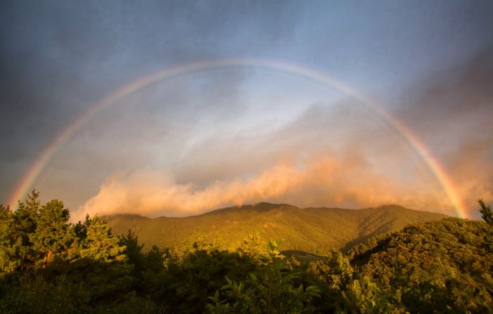 A beautiful landscape with a full bow of the rainbow above - rainbow photography tips