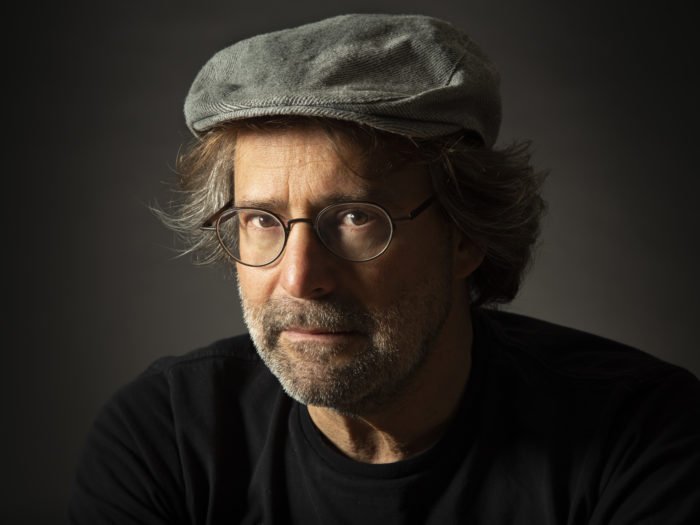 A close-up studio headshot of a man wearing a hat and glasses using Rembrandt portrait lighting
