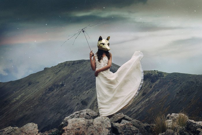 Tipos de fotografía de retrato- un retrato conceptual de una modelo femenina con una máscara de lobo parada en un paisaje montañoso