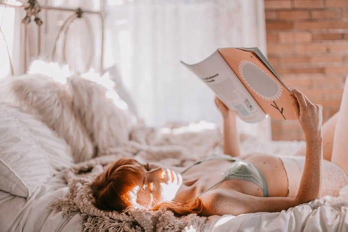 Boudoir portrait of a woman laying on a bed and reading a book 