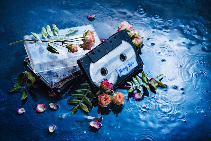 A creative flat lay of flower petals and cassette tapes on a hand painted background 