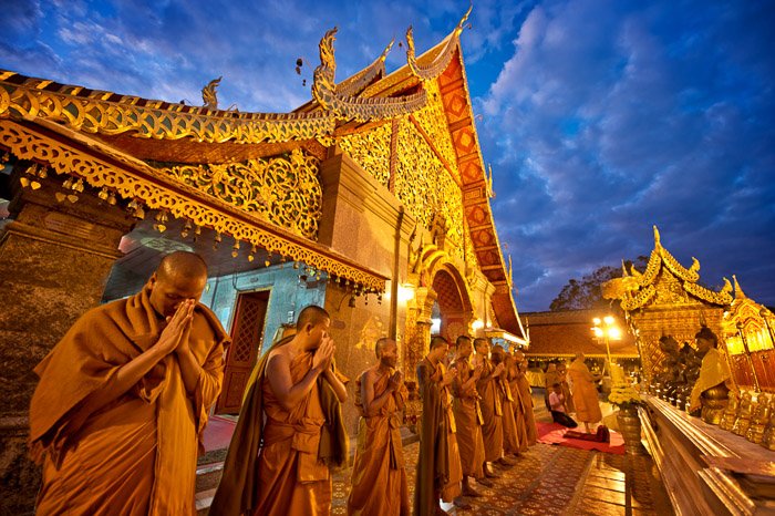A line of Buddhist monks praying outside a temple at dusk - shallow vs deep depth of field