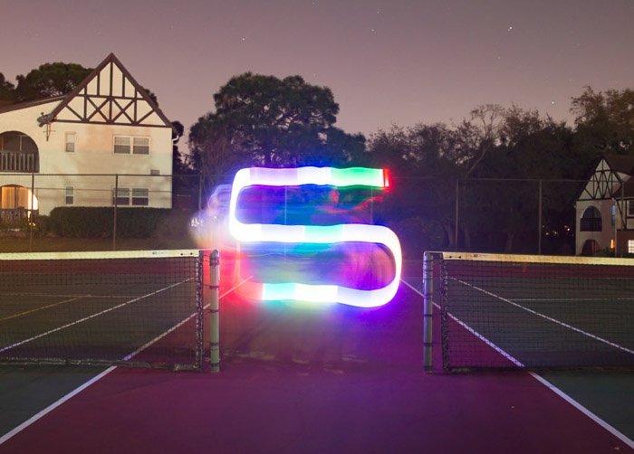 A colorful S shaped streak of light painting shot under on a tennis court at night using LED light painting tools