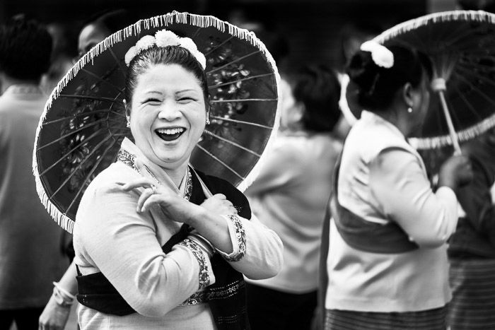 A black and white street portrait of a woman with an umbrella laughing with friends before the start of the annual flower parade. Narrative photography tips