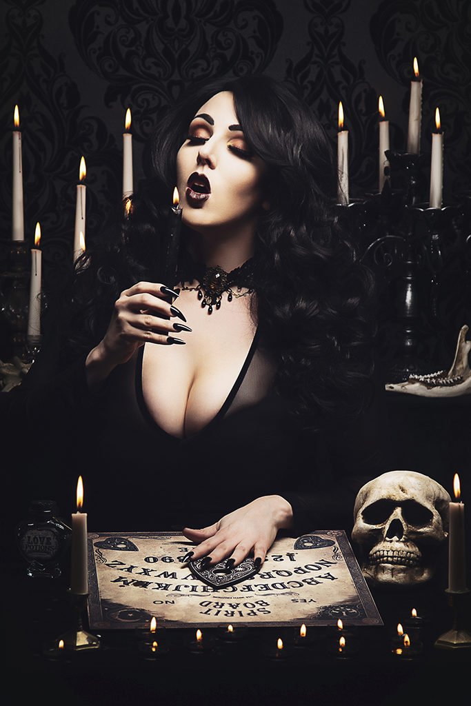 Boudoir self portrait of a goth woman surrounded by candles with parchment and a skull on a table