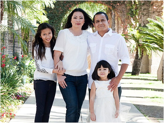 A family of four posing outdoors in dappled light