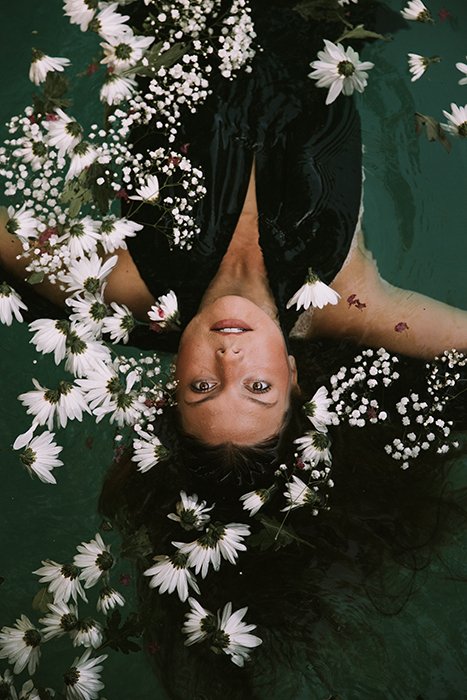 Dreamy photo of a female model posing in water surrounded by white flowers