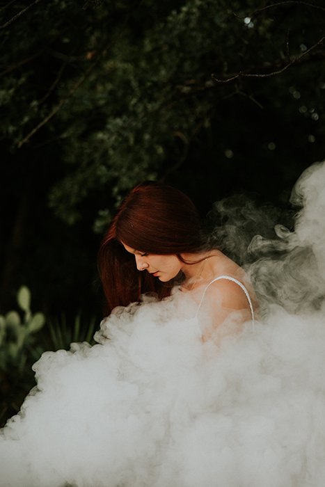 Retrato sonhador de um modelo feminino posando ao ar livre cercado por fumaça e um fundo sonhador