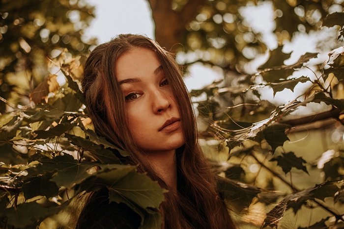 Dreamy photography shot of a female model posing outdoors among leaves - ethereal portraits 