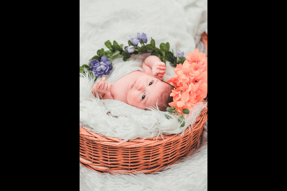 A baby in a basket with bedding and flowers as one of the examples of Easter picture ideas