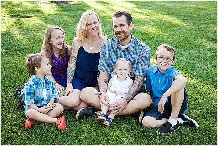 A smiling family of six, posing outdoors sitting on the grass - emotional photography