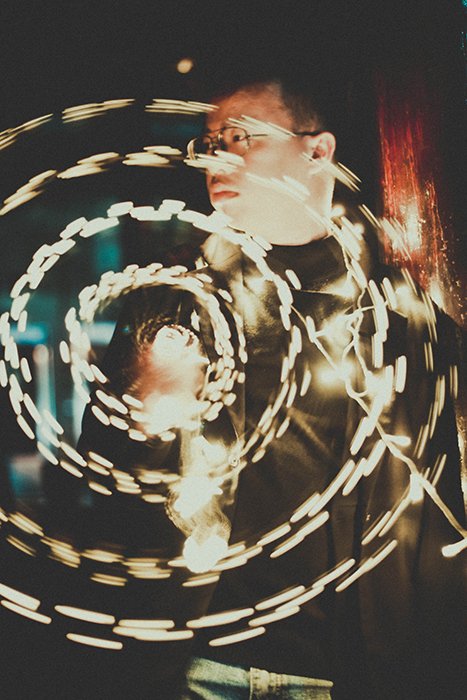 creative long exposure portrait of a man posing outdoors, with circles of fairy lights in front of him