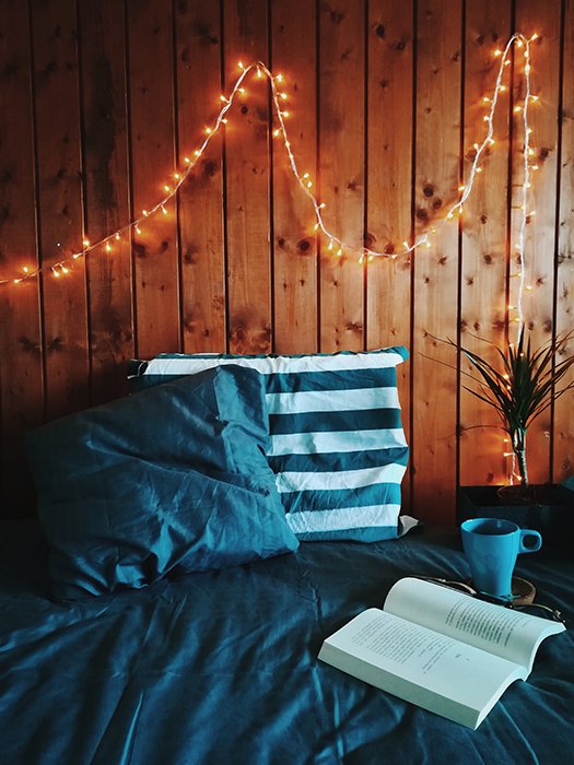 A still life shot of a book and cup on a bed with fairy lights on the wall - fairy light photography