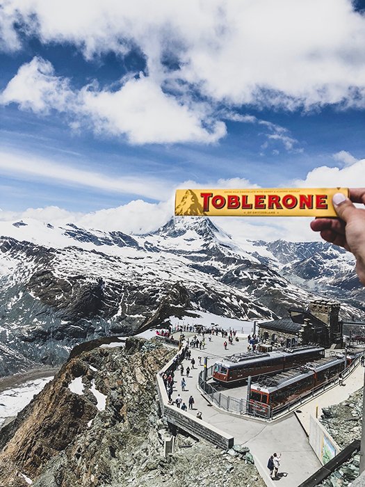 A person holding a toblerone chocolate bar over a mountainous landscape 