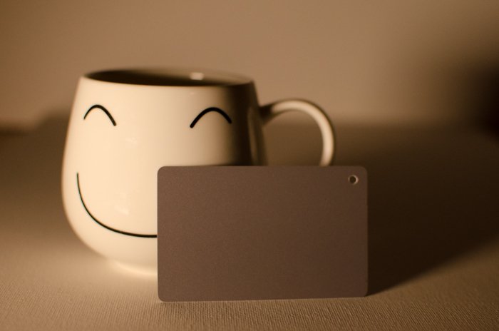 A smily face mug on a neutral background beside a photography grey card for color balance