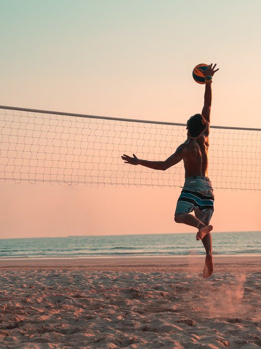 A portrait of a person playing volleyball on the beach at sunset 