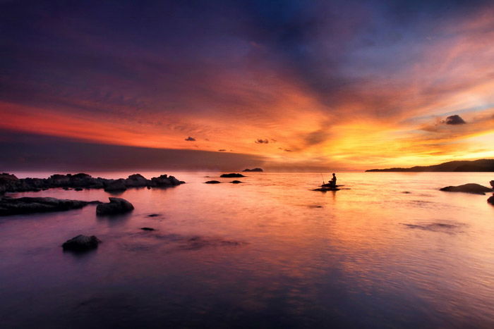 A beautiful minimalist landscape with a fisherman silhouetted against the sunset sky.