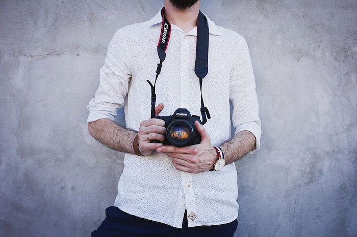 an image of a photographer holding a Canon DSLR camera standing against a grey wall