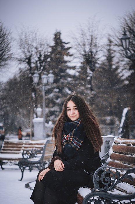 Atmospheric winter portrait of a female model posing on a bench in the falling snow