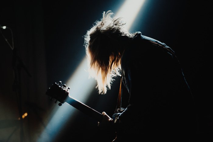 A silhouette of a guitarist performing with a shaft of light shining in the background providing backlight and rim lighting