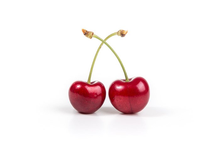 A close up of two cherries on white background