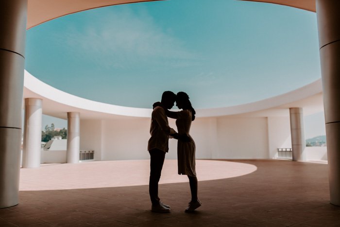 A couple embracing in an open-domed space with pillars under a blue sky