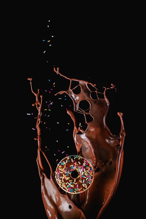 A chocolate doughnut in the foreground of a delicious chocolate splash 