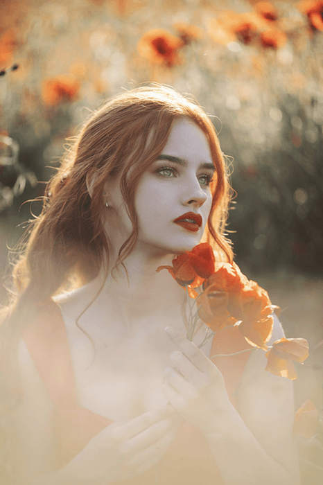 a dreamy portrait image of a red haired model in a field of roses