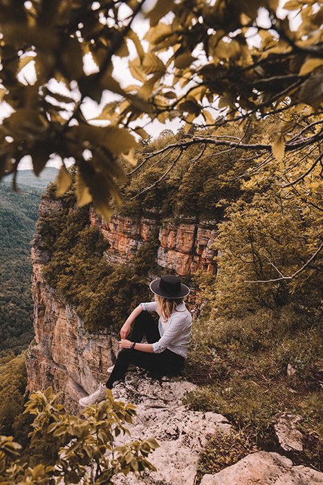 An outdoor portrait of a female model sitting on rocks amidst a beautiful mountainous autumn landscape.