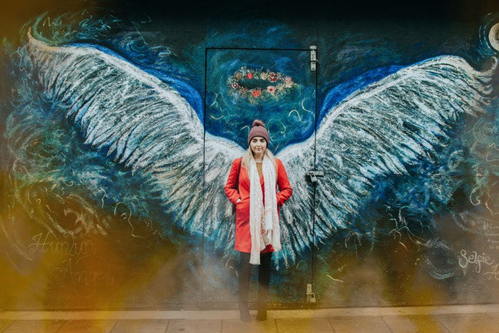 Woman standing in front of wall with angel wings drawn onto it 