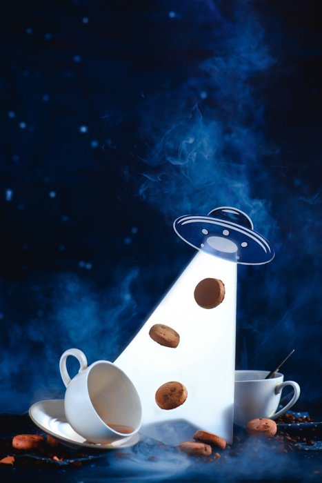 An outer space themed food still life including coffee cups, sugar ,cookies and a flying saucer