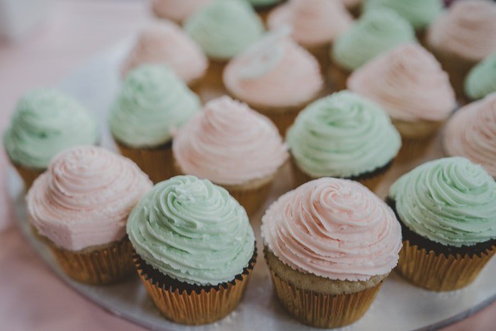 Bright photo of a plate of pink and green frosted cupcakes against a light background